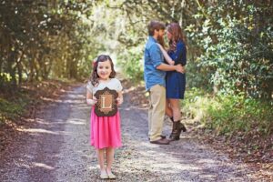 Girl holding L sign with couple in background