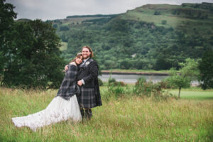a bride wearing a tartan shawl with a groom wearing matching tartan in the grounds of Mar Hall