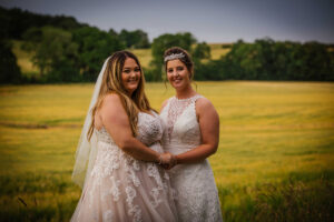 two smiling brides standing next to a field