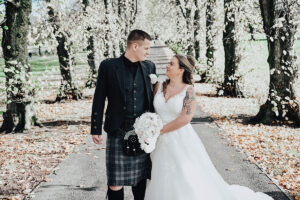 A bride and groom look at each other while walking along a tree-lined path