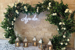 A foliage and rose ceremony arch with neon Aye Do sign from Lights Candy Action
