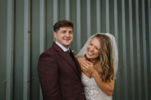 a bride and groom laughing against a green ribbed metal wall