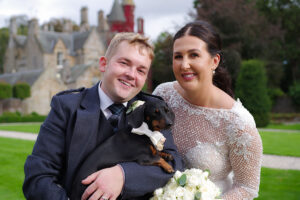 a bride and groom pose with a Dachshund outside Carlowrie Castle