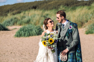 a bride and groom wearing sunglasses walking along a beach