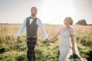 a bride and groom walking hand in hand through at field in sunshine at Harelaw Farm